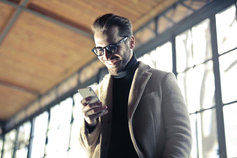 A man in a coat smiling at the phone in his hand